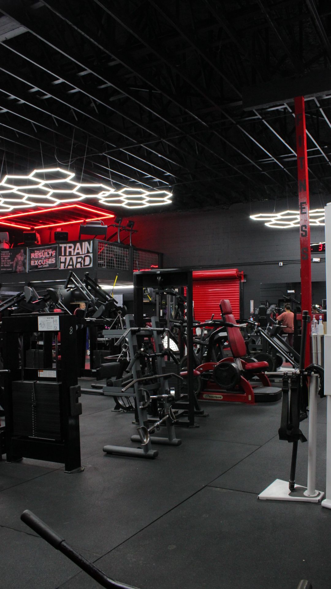 Red-lit gym interior with weight machines, benches, and hexagonal ceiling lights