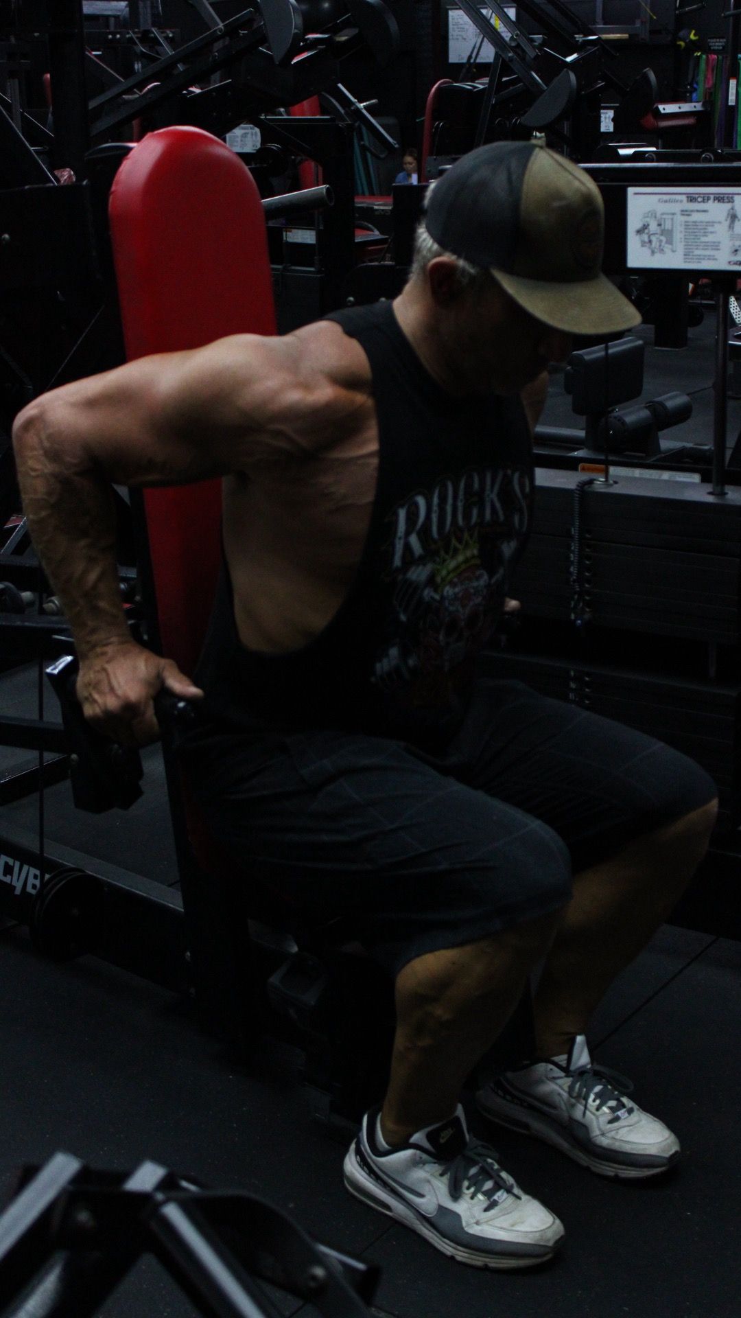 Person in a gym holding dumbbells with a trainer standing behind them