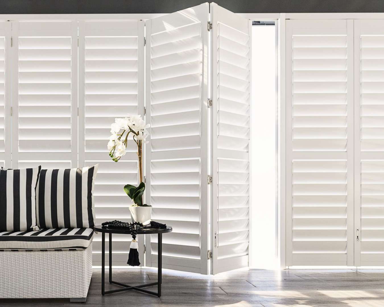 A living room with a couch , table and shutters on the windows.