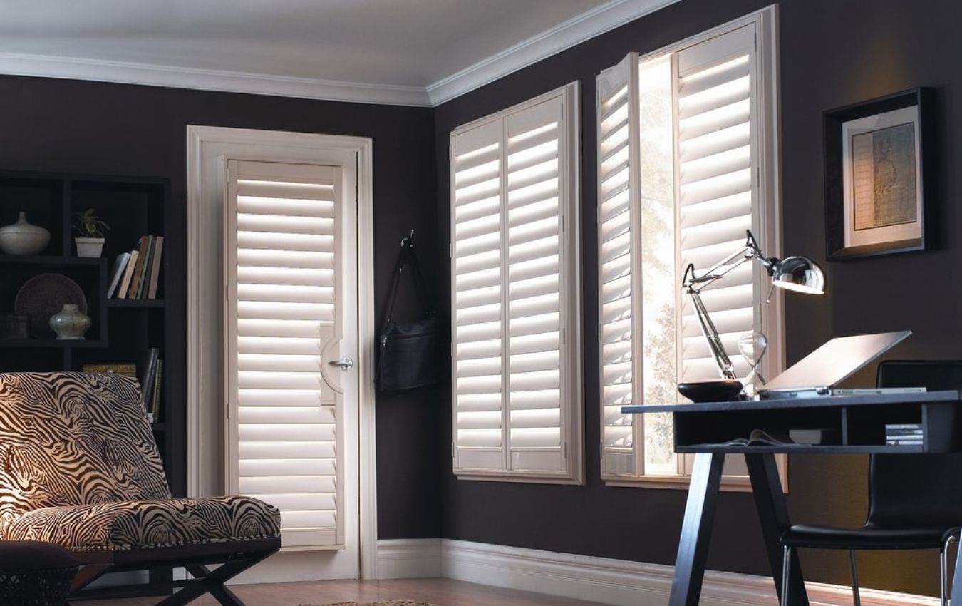 A living room with dark walls and white shutters on the windows