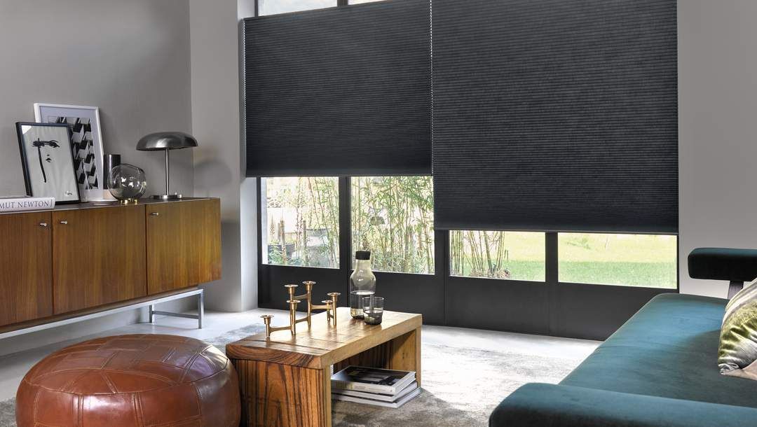 A living room with a blue couch , ottoman , coffee table and black blinds.