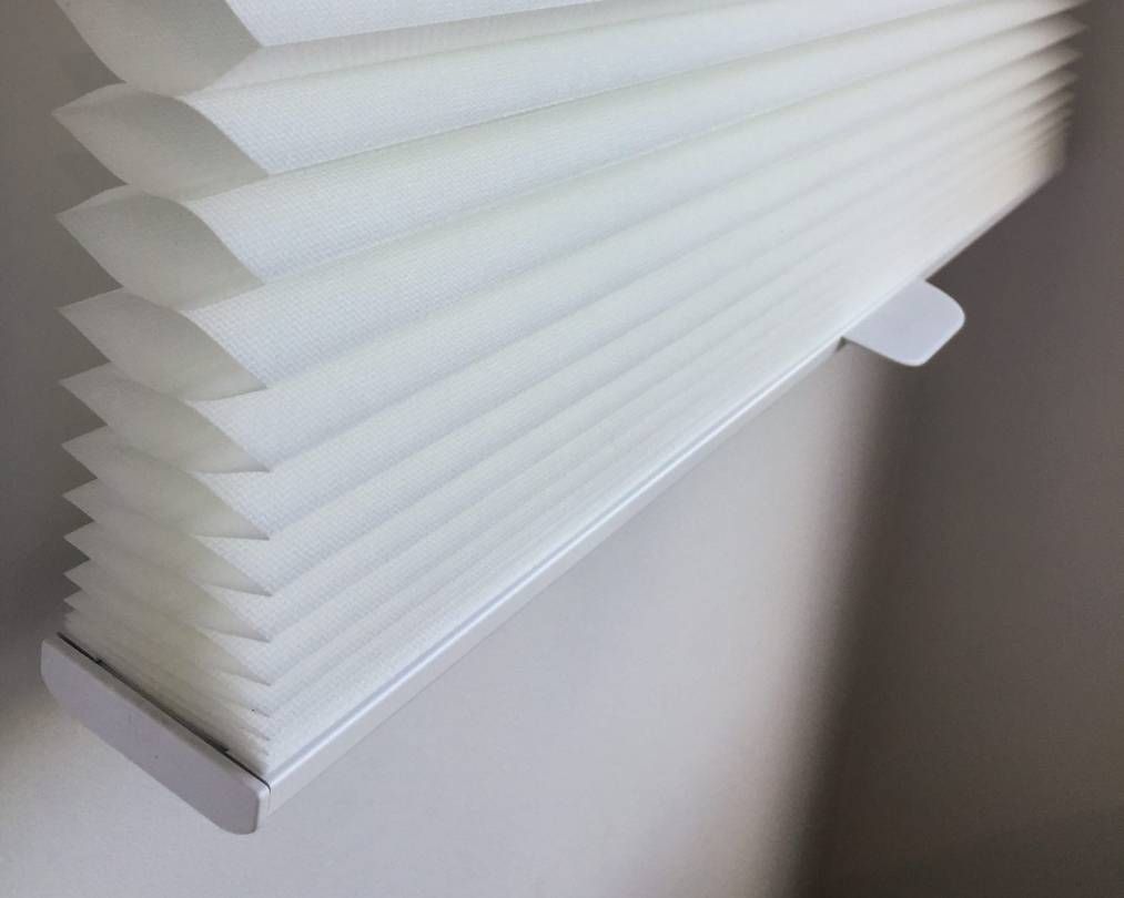 A close up of a white pleated blind on a window.
