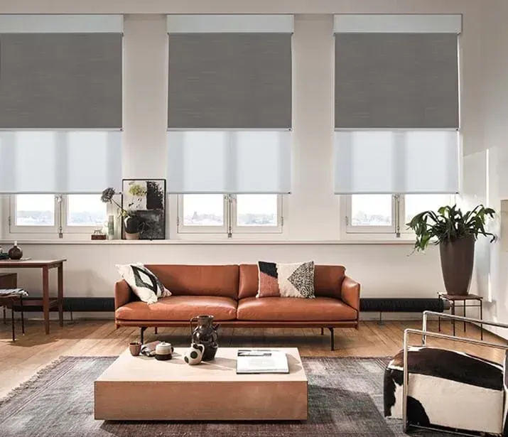 A living room with a brown couch , a coffee table , chairs , and gray blinds.