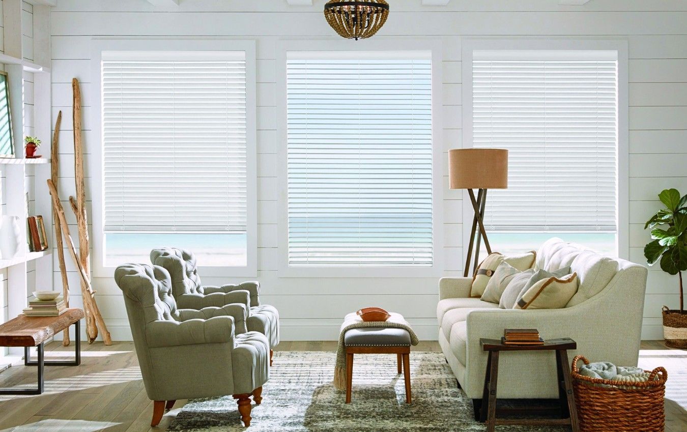 A living room with a couch, venetian blinds, chairs , and a lamp.