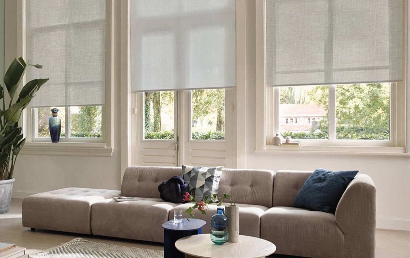 A living room with a couch , two tables , and two windows and blinds.