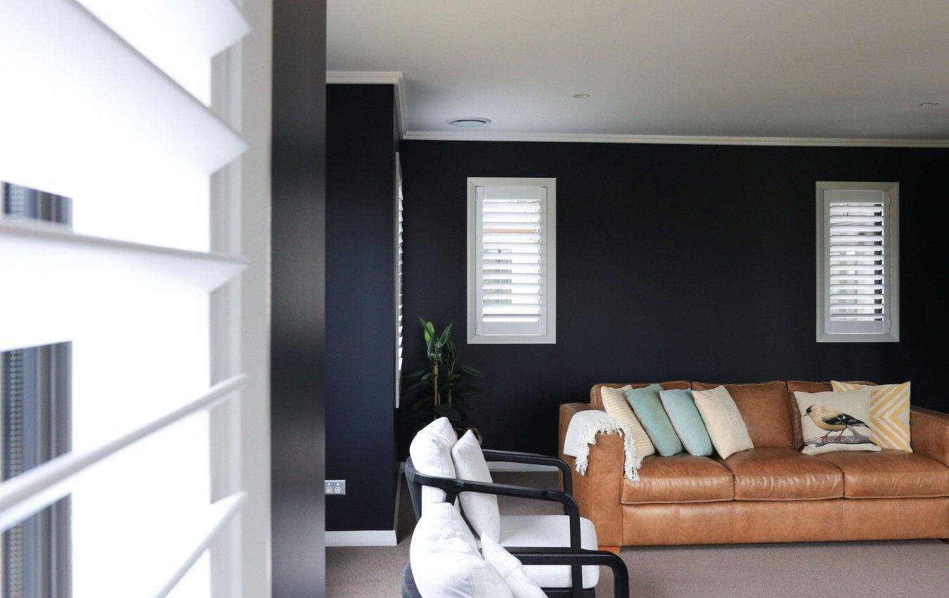 A living room with a brown couch and two chairs, shutters
