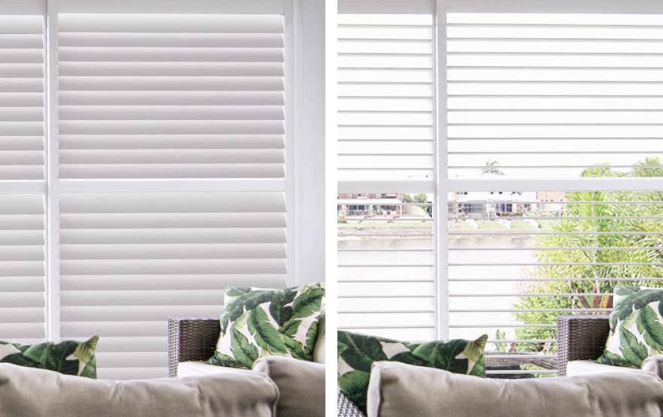 A living room with white shutters on the windows and a couch.