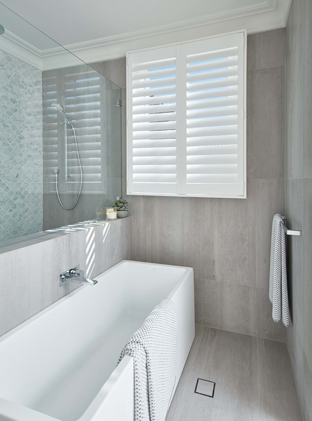 A bathroom with a bathtub , shower , mirror and shutters.