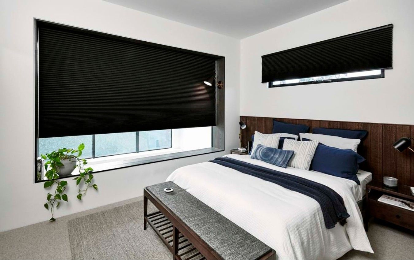A bedroom with a bed and a window with black blinds.