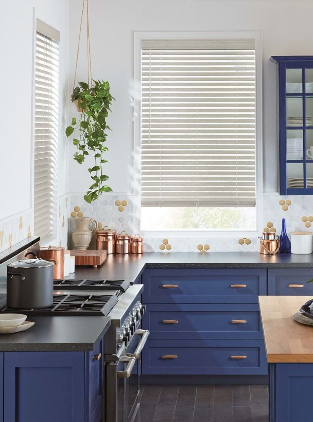 A kitchen with blue cabinets , a stove , and a window with blinds.