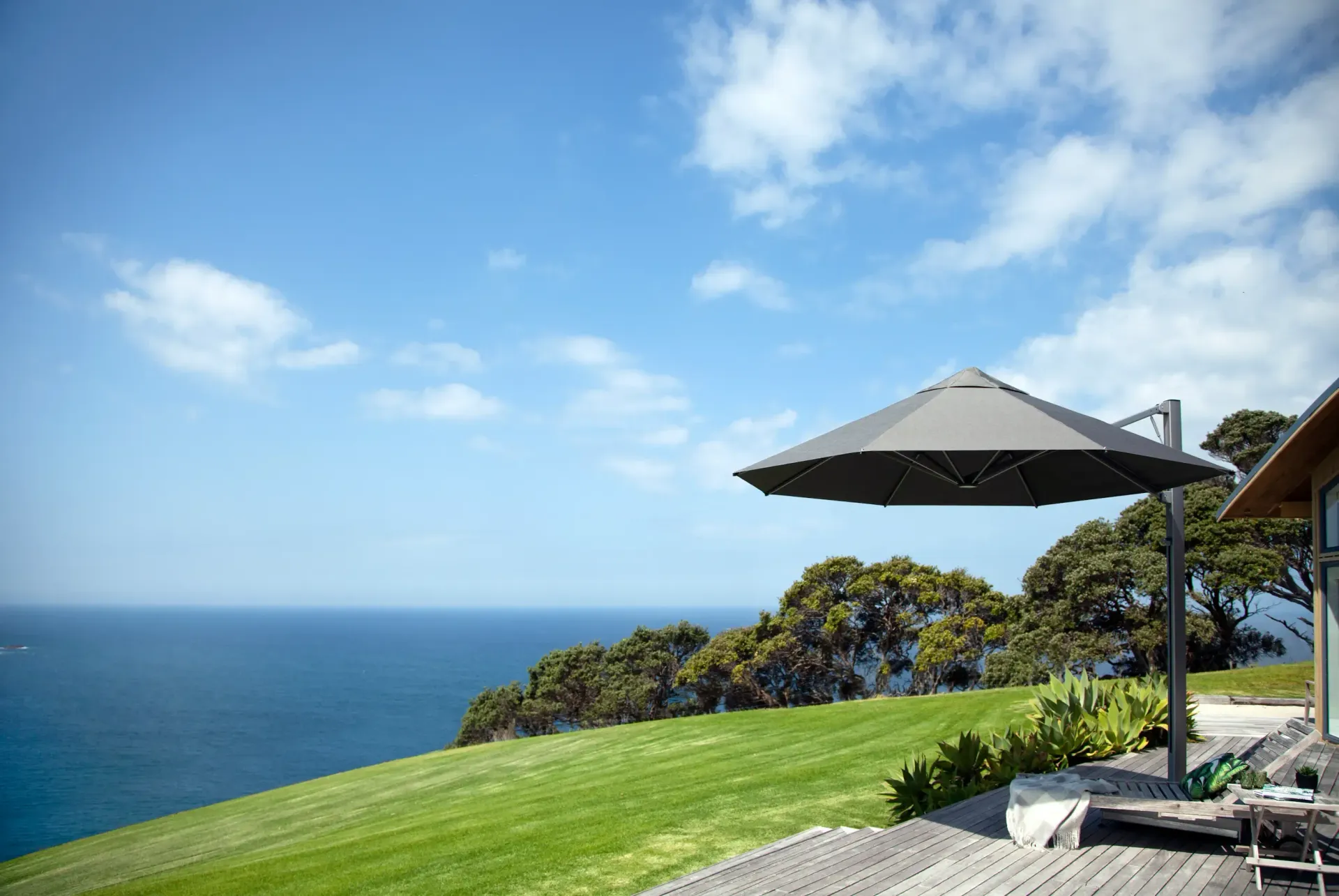Outdoor patio with retractable awning overlooking the ocean, featuring modern furniture and potted plants.