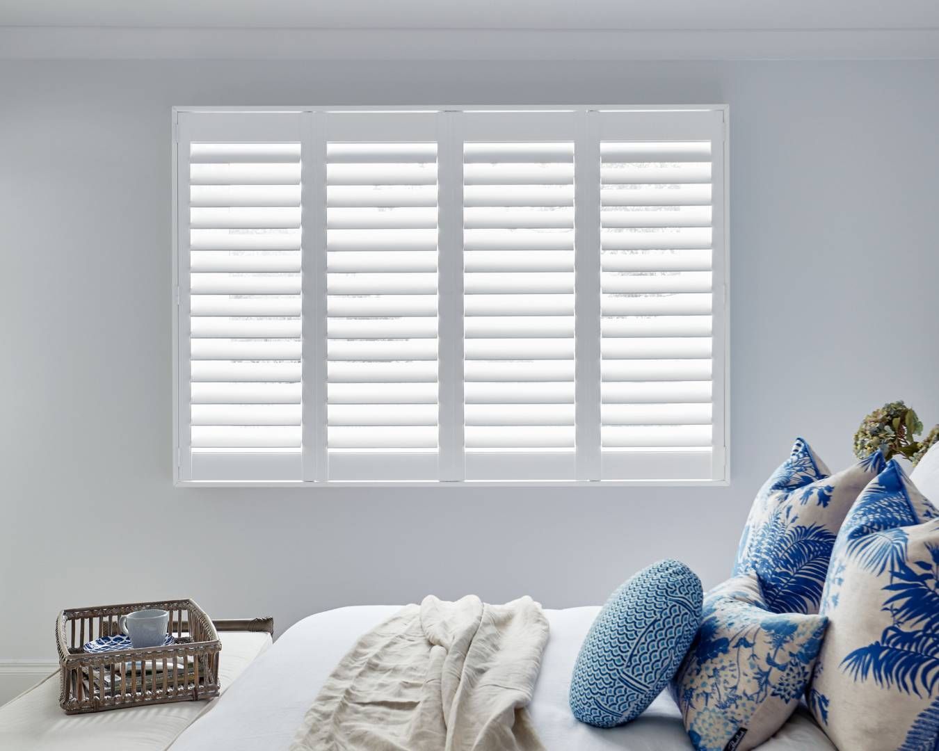 A bedroom with a bed , pillows and a window with white shutters.