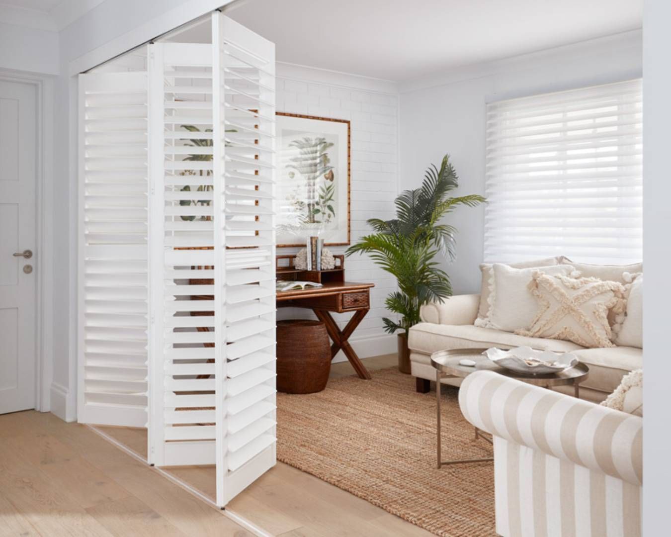 Bright living room with white shutters, a comfortable sofa, and indoor plants.