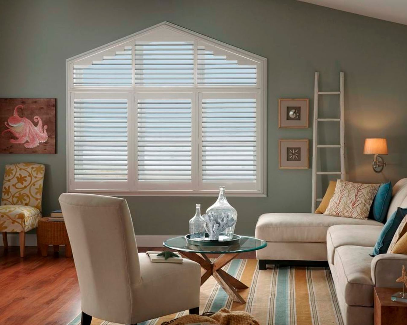 A living room with a couch , chair , coffee table and large window with shutters.