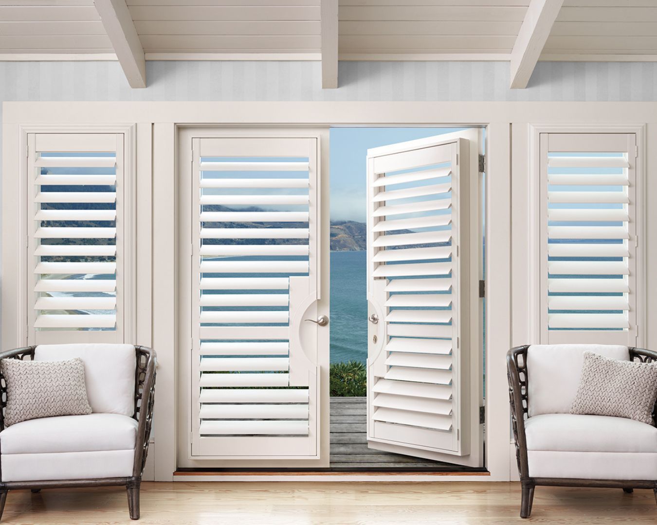 A living room with two chairs and a large window with shutters open.