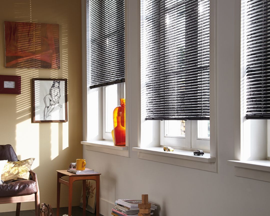 A living room with blinds on the windows and a chair