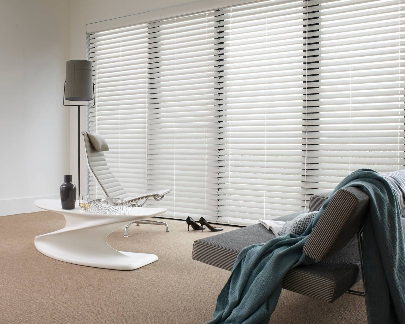 A living room with a chair , table , and blinds on the windows.