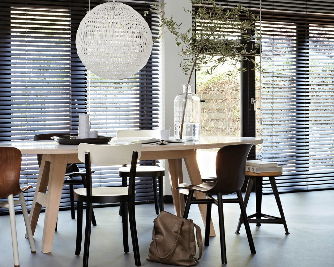 A dining room with a table and chairs and blinds on the windows.