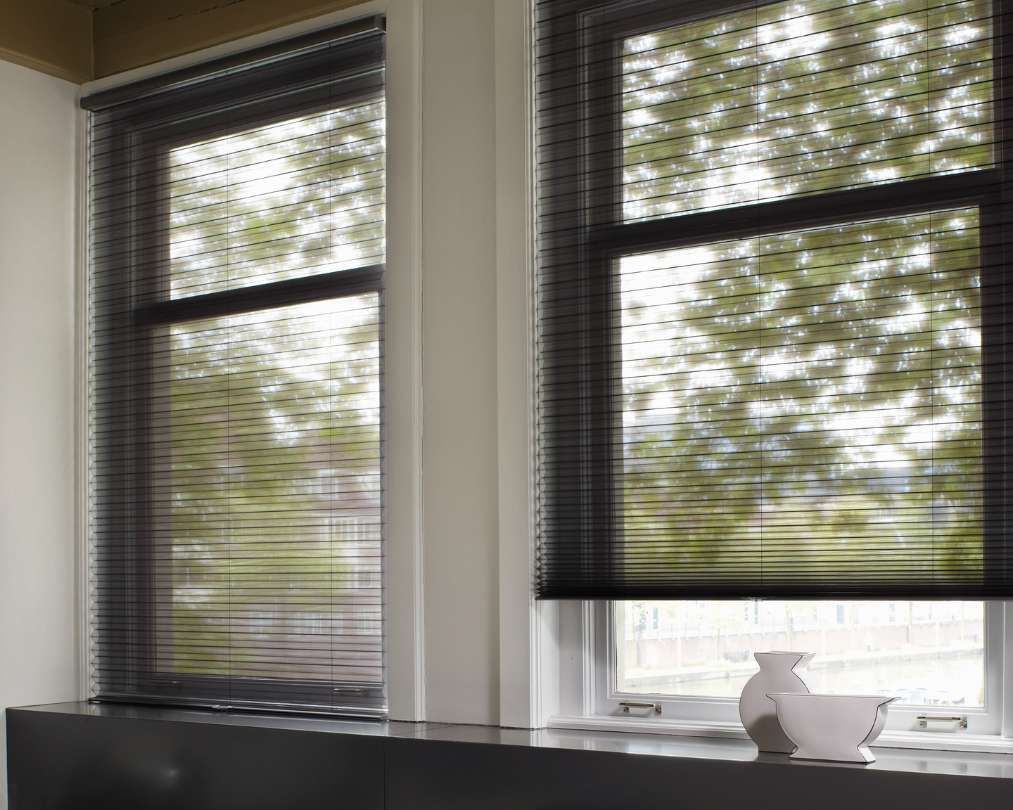 Two windows with black blinds and a vase on the window sill.