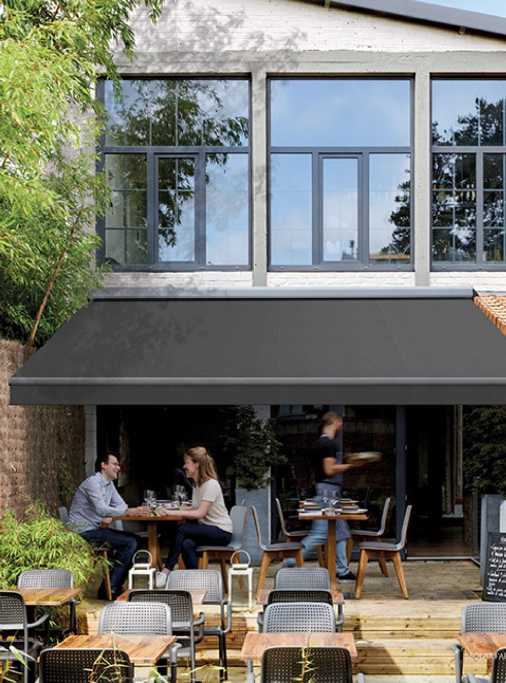 A group of people are sitting at tables under an awning outside of a restaurant.