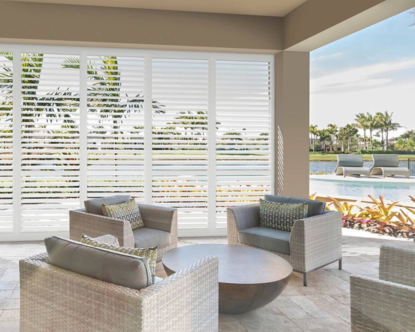 A living room with chairs and a table with shutters on the windows
