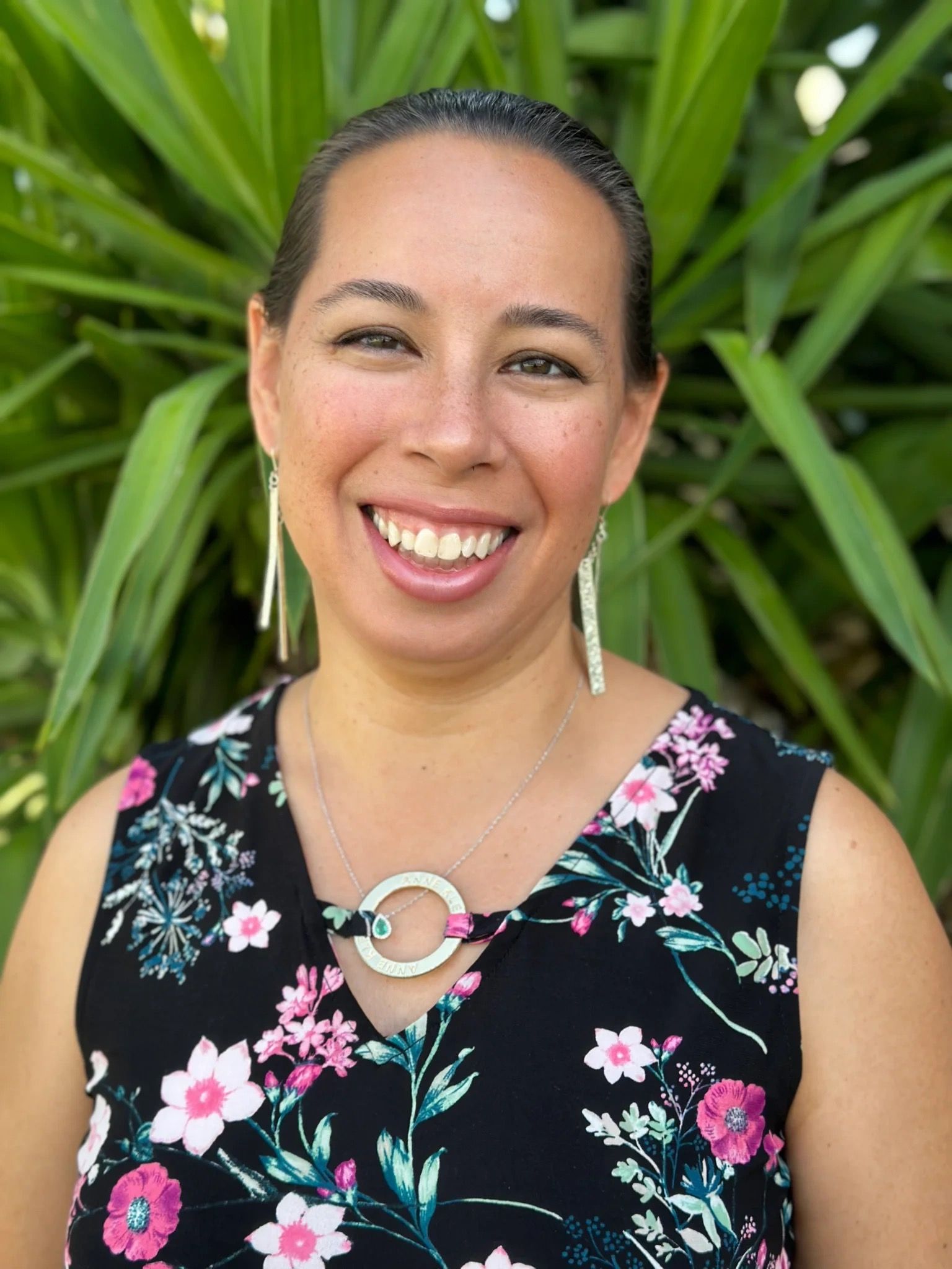 A woman wearing a floral shirt and earrings is smiling for the camera.