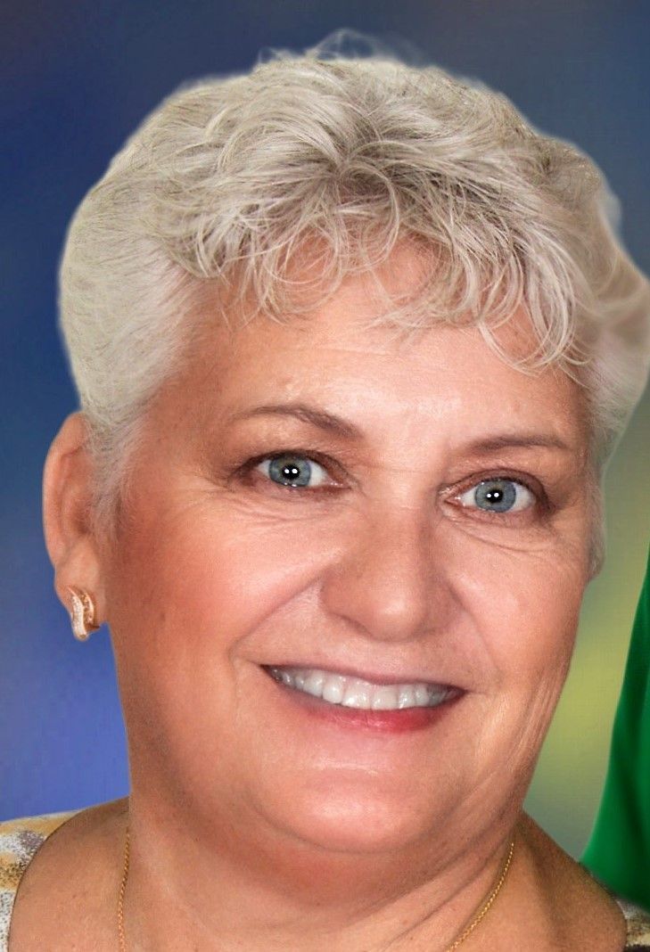 A woman with short white hair and blue eyes is smiling for the camera.