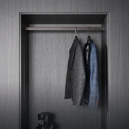 Armario abierto con tres chaquetas colgadas en una barra y una bolsa para la cámara en el suelo.