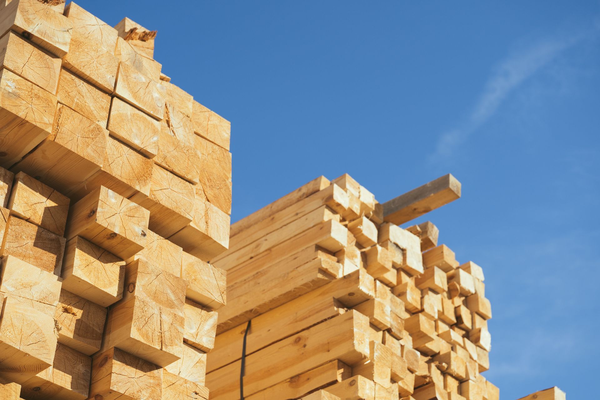 Stacks of cut lumber piled outdoors against a clear blue sky. Stacks of cut lumber piled outdoors against a clear blue sky.