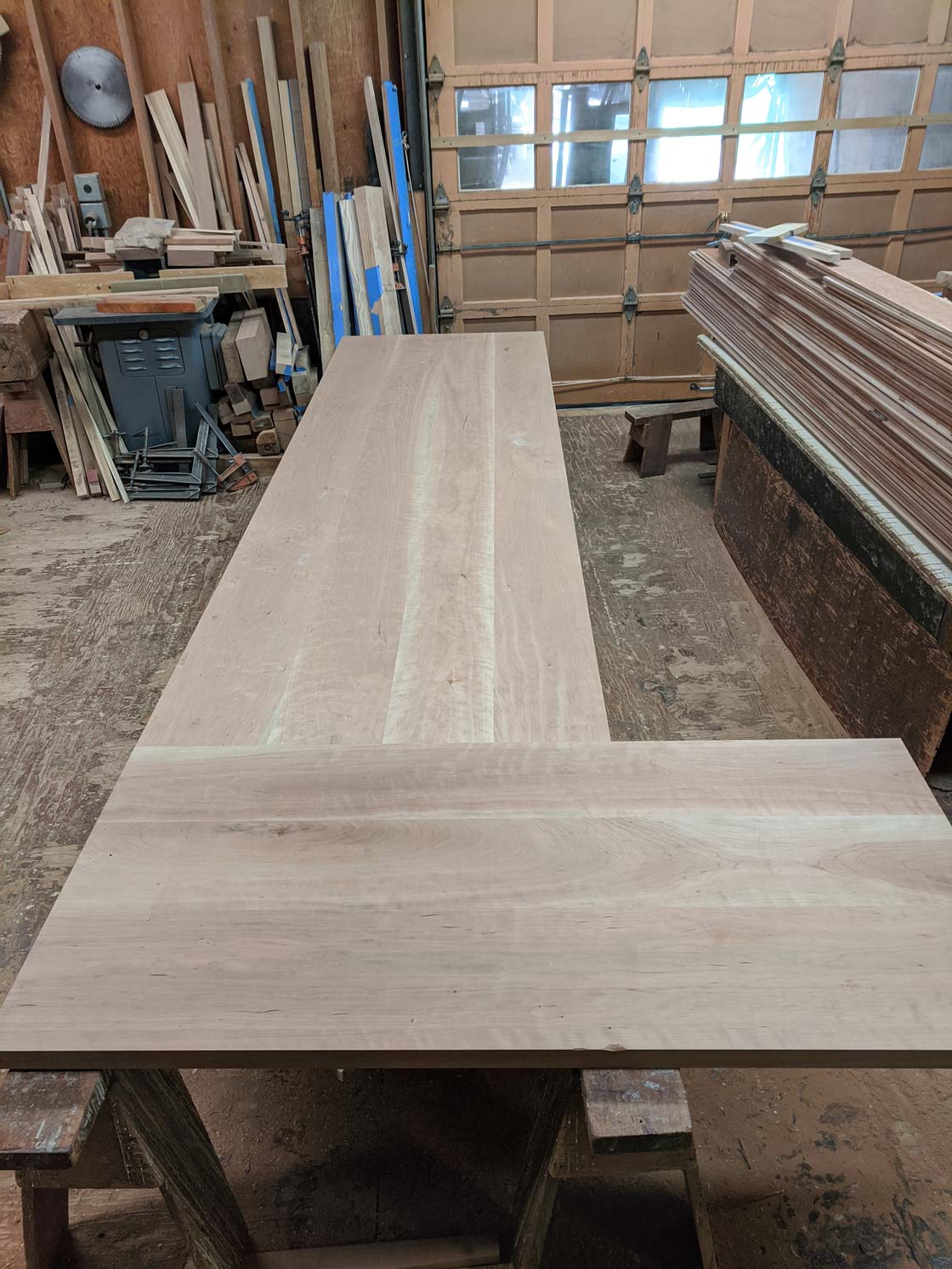 L-shaped unfinished wooden tabletop in a workshop.