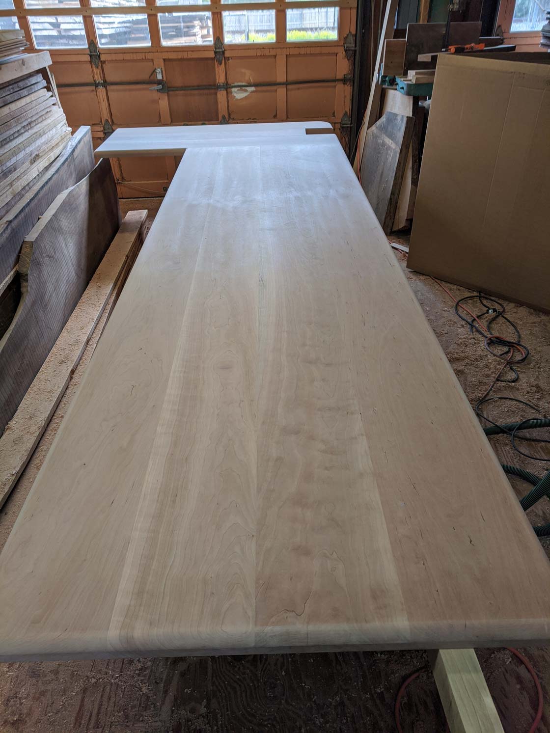 Long, light-colored wooden countertop in a workshop.  The counter is unfinished with a corner cut out.