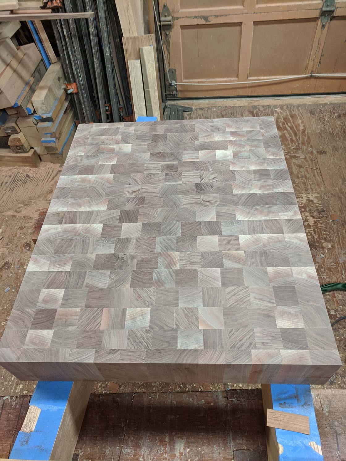 Butcher block tabletop made of end-grain wood, resting on two blue-taped supports in a workshop.