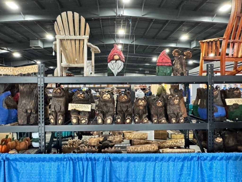 Display of wooden sculptures, including bears and gnomes, at a craft fair, set on shelves with a blue skirted table.