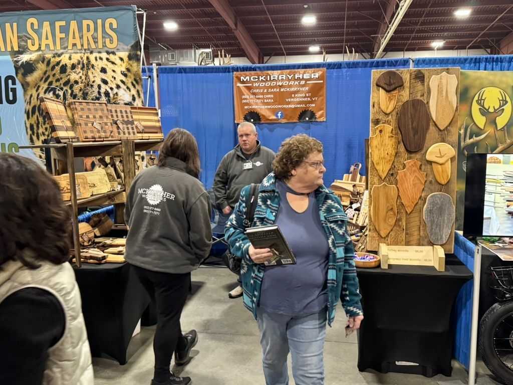 People browsing vendor booths at a trade show. Wood crafts are displayed, along with a banner for African safaris.