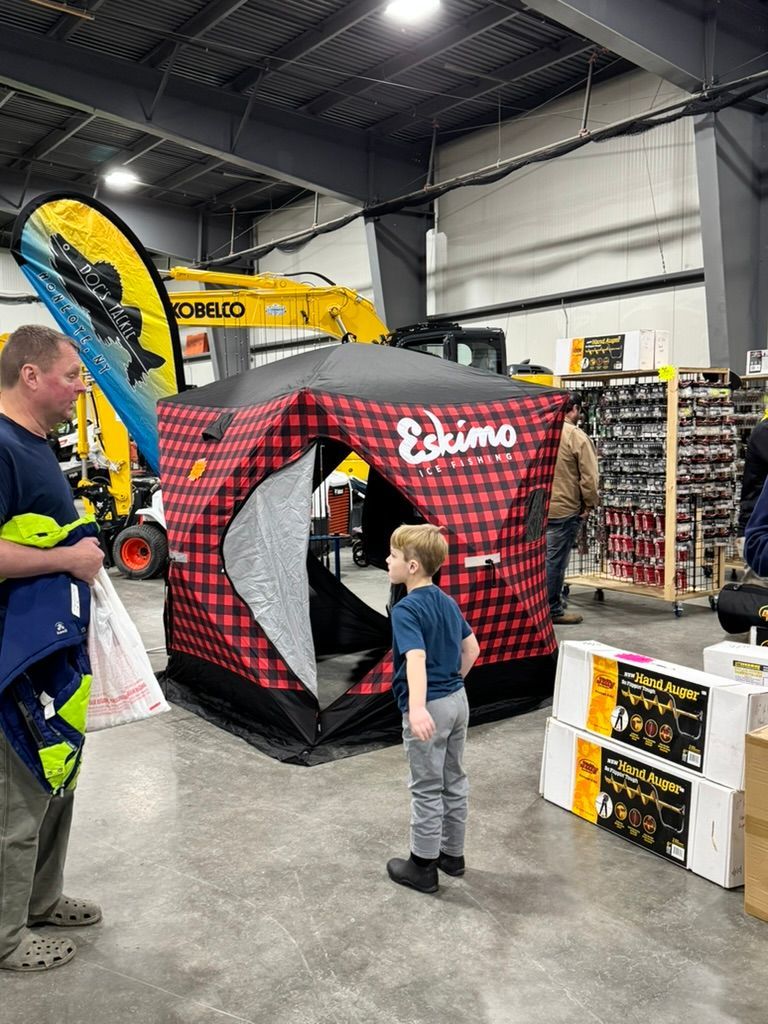 Man and child looking at an Eskimo ice fishing shelter at an indoor event, with construction equipment visible.
