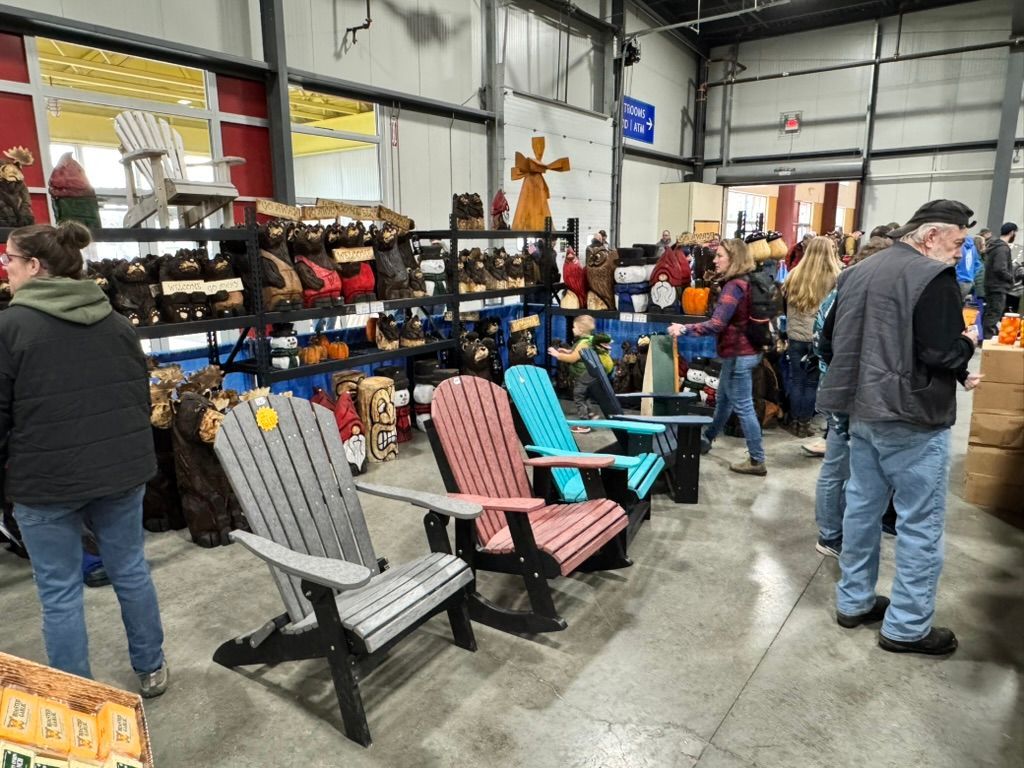 Indoor craft fair with wooden crafts, colorful chairs, and shoppers.
