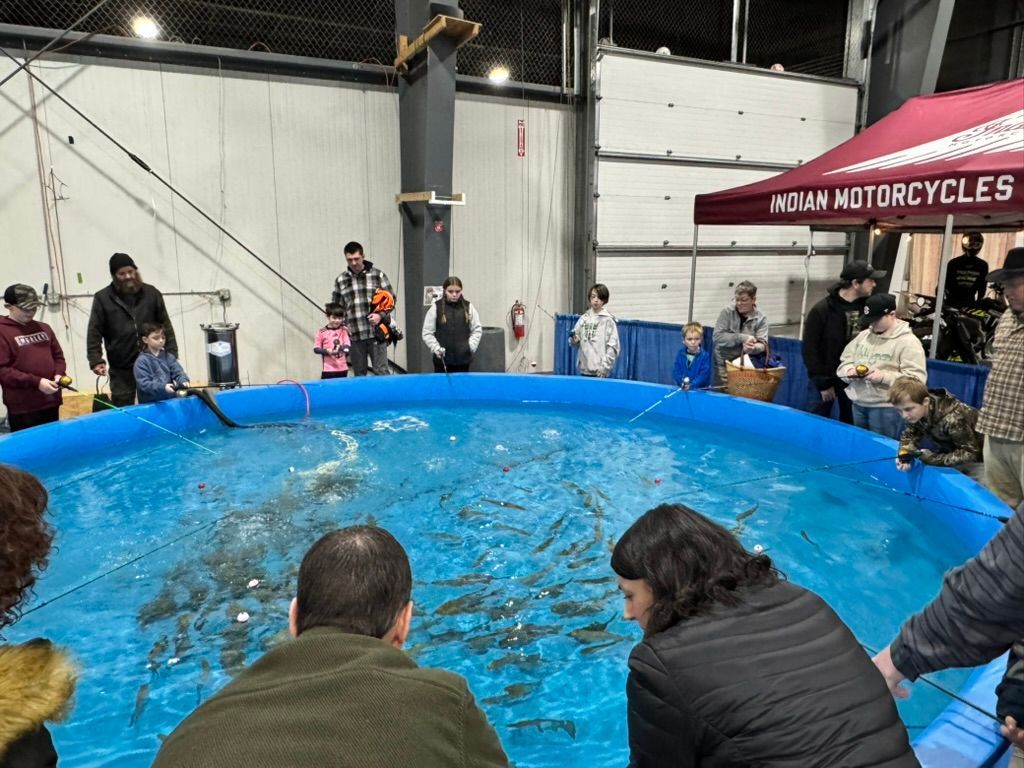 People fishing in a blue pool at an indoor event. Others watch. A motorcycle booth is visible.