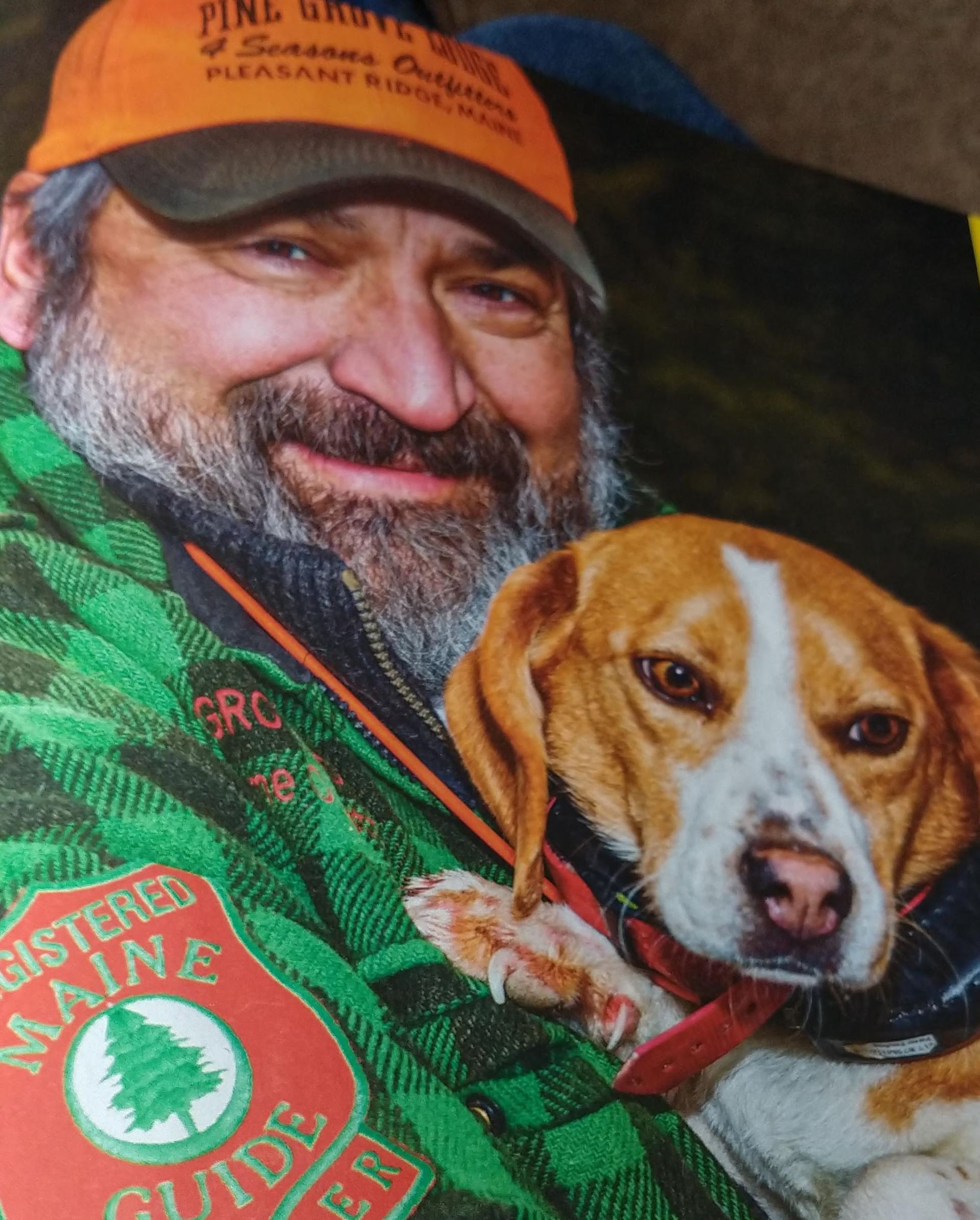 Man in orange hat with a beagle dog. They're both smiling. Man's jacket says 