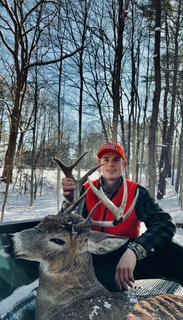 Hunter in orange vest holding deer antlers in snow-covered woods.