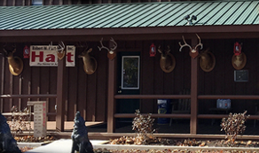 Exterior of a hunting lodge with mounted deer heads above a porch and sign.