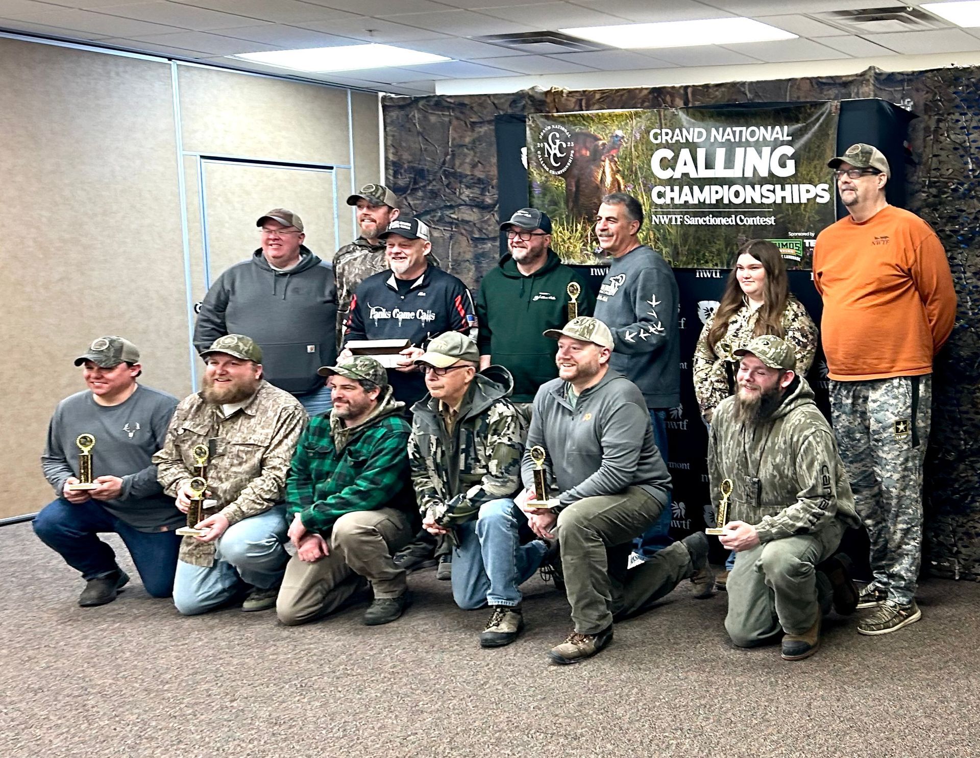 Group of people at the Idaho National Calling Championships, holding trophies. Some are wearing camouflage clothing.