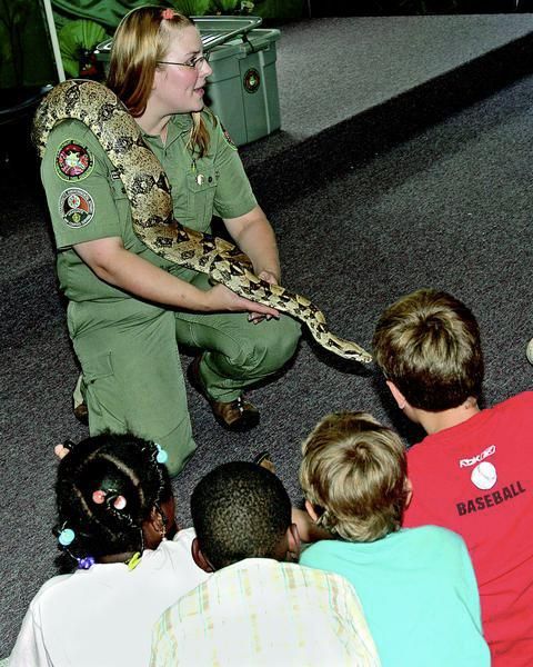 Woman in uniform shows a large snake to a group of children.