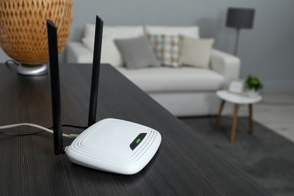 White Wi-Fi router with black antennas on a dark wood table; living room in background — D-stress Computers In Idalia, QLD