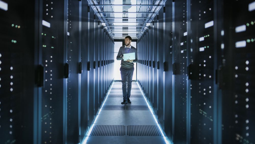 A Man Is Standing In A Server Room Looking At A Laptop — D-stress Computers In Idalia, QLD