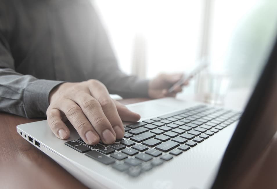 A Man Is Typing On A Laptop Computer While Holding A Cell Phone — D-stress Computers In Idalia, QLD
