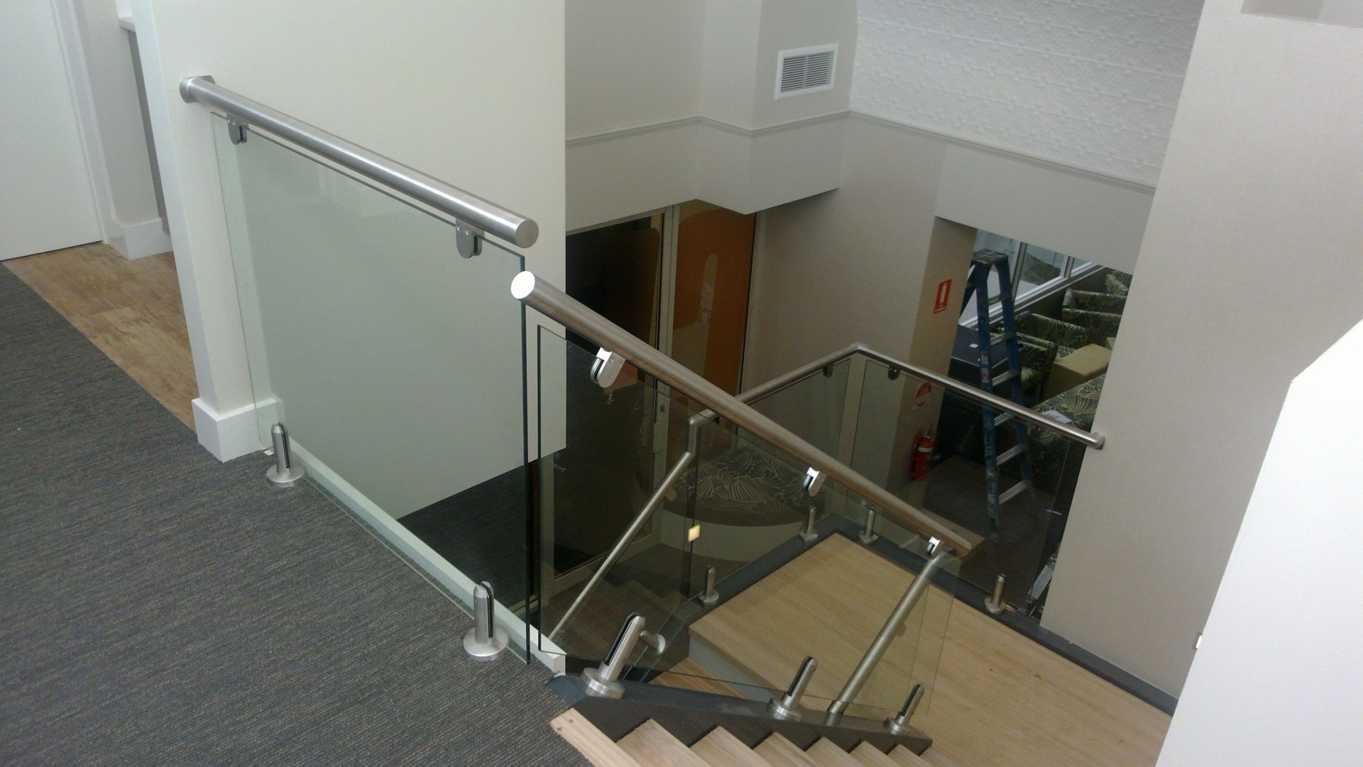 Stairwell with glass railing and metal handrail overlooking a lower floor landing