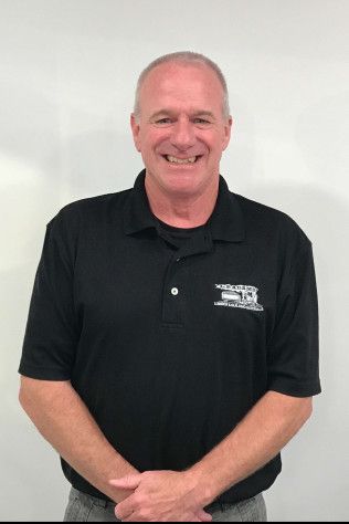 Smiling man in a black polo shirt standing against a plain white background