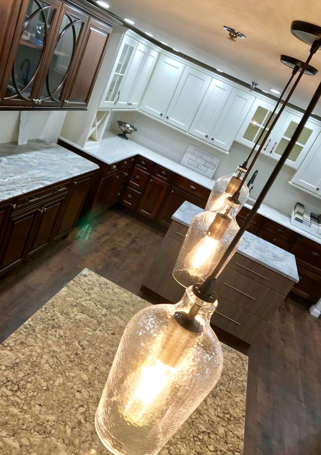 Modern kitchen with white cabinets, dark wood floors, granite counters, and a hanging glass pendant light
