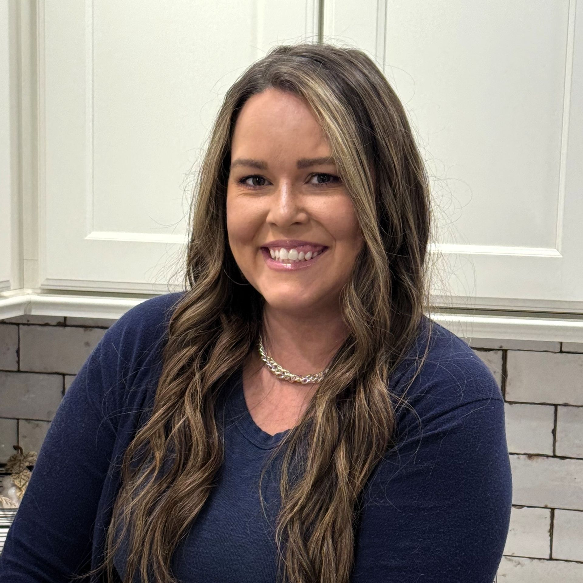 Smiling woman in a navy top and necklace standing in a bright kitchen