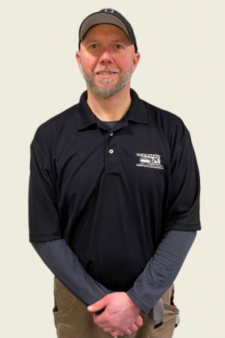 Smiling man in black polo and cap standing against a plain wall